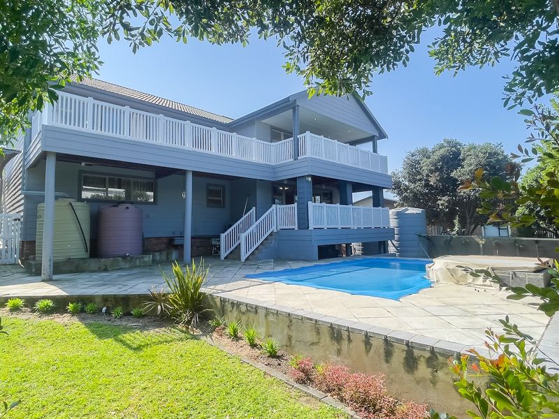 Rear exterior view featuring a swimming pool, paved patio area, and a multi-level deck with white balustrades overlooking the garden.