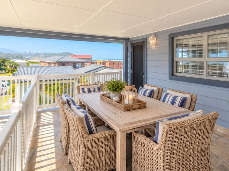 A spacious covered balcony featuring tiled flooring, white balustrades, and recessed lighting, offering an ideal outdoor dining area with pleasant neighborhood views.