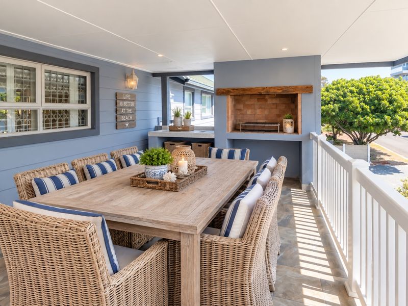 A well-maintained covered patio featuring a built-in brick fireplace, tiled flooring, and a protective railing, ideal for outdoor dining and entertainment.