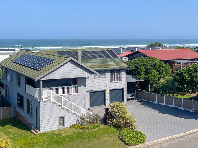 Elevated view of a two-story coastal home featuring solar panels, a double garage, paved driveway, and an external staircase leading to an upper balcony.