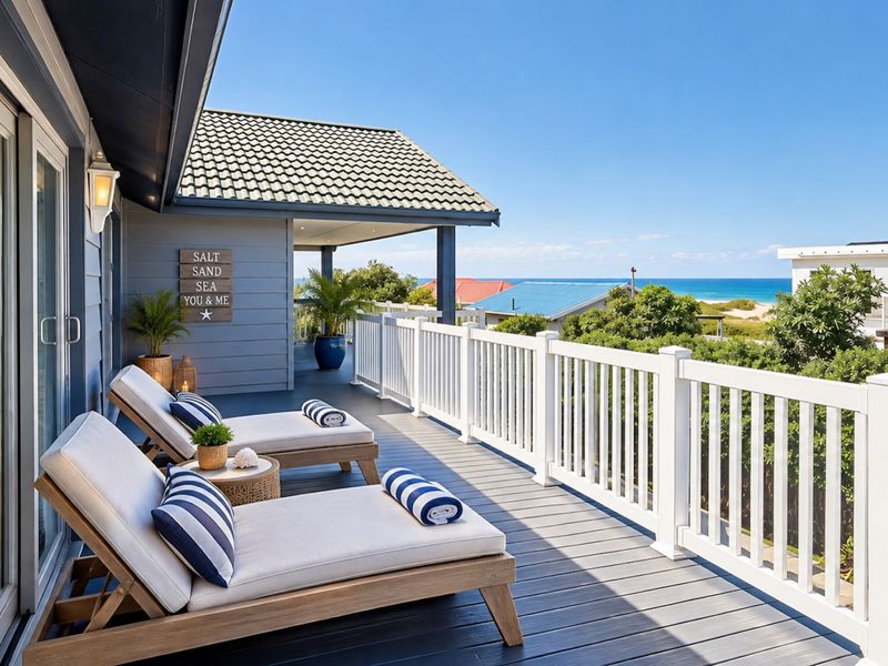 A spacious covered balcony featuring timber decking, white balustrades, and expansive ocean views, providing an ideal outdoor relaxation space.