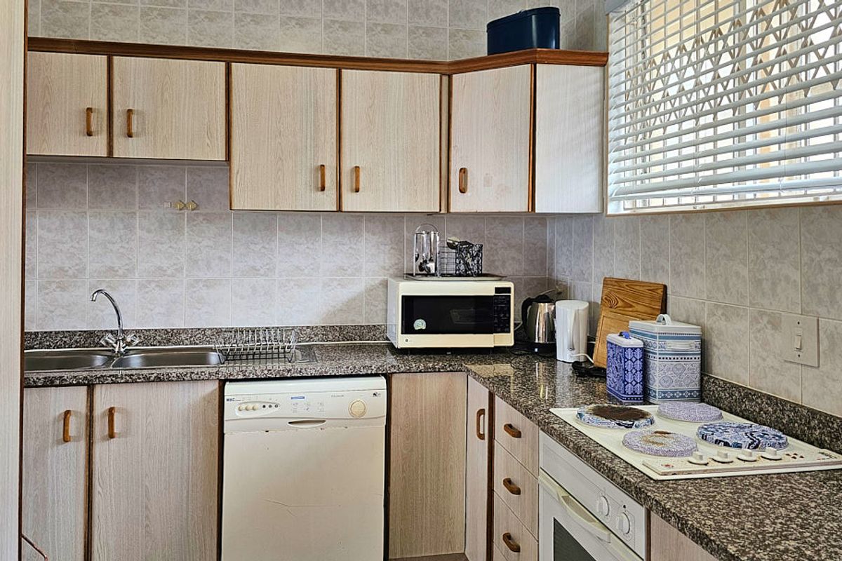 A functional kitchen featuring granite countertops, laminate cabinetry, a built-in oven, and an electric hob, with a tiled backsplash and window blinds.