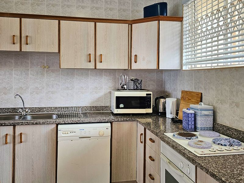 A functional kitchen featuring granite countertops, laminate cabinetry, a built-in oven, and an electric hob, with a tiled backsplash and window blinds.