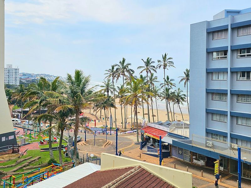 Elevated coastal view overlooking the beach, palm trees, and surrounding apartment buildings.