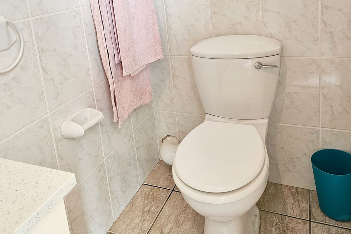 A functional bathroom featuring tiled walls and flooring, equipped with a standard toilet and wall-mounted fixtures.