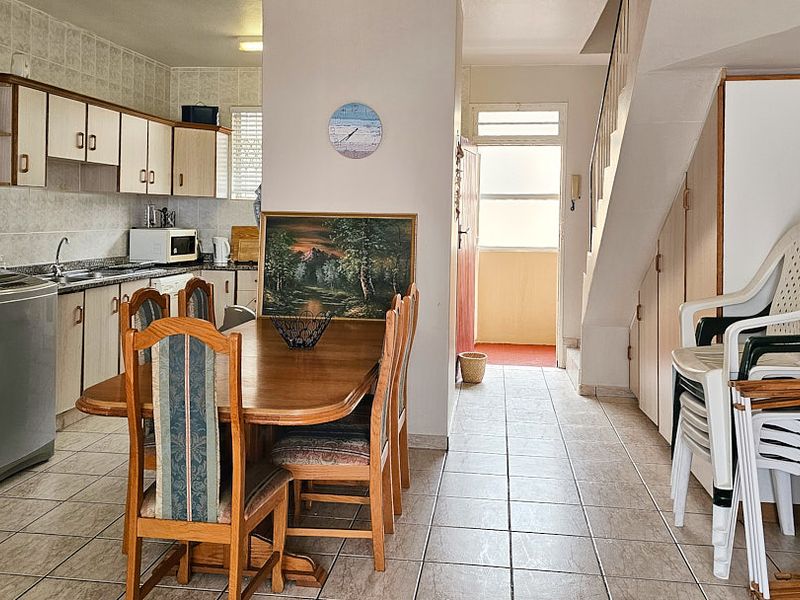 Open-plan kitchen and dining area featuring tiled flooring, built-in cabinetry with granite countertops, and an adjacent staircase with integrated under-stair storage.