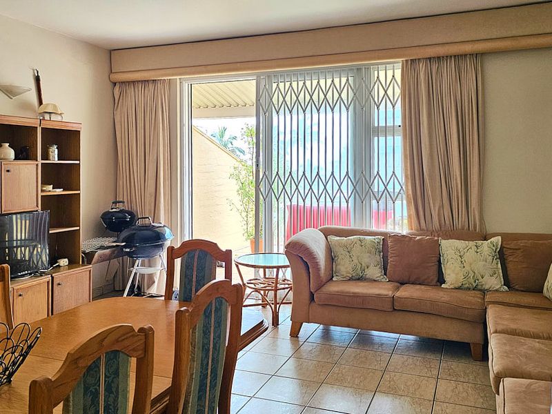 Open-plan living and dining area featuring tiled flooring, a wall-mounted air conditioner, and sliding glass doors leading to an outdoor space.