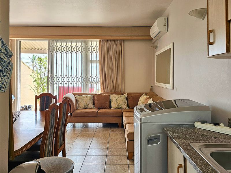 Open-plan living and kitchen area featuring tiled flooring, split-system air conditioning, and direct access to an outdoor patio through a security-gated sliding door.