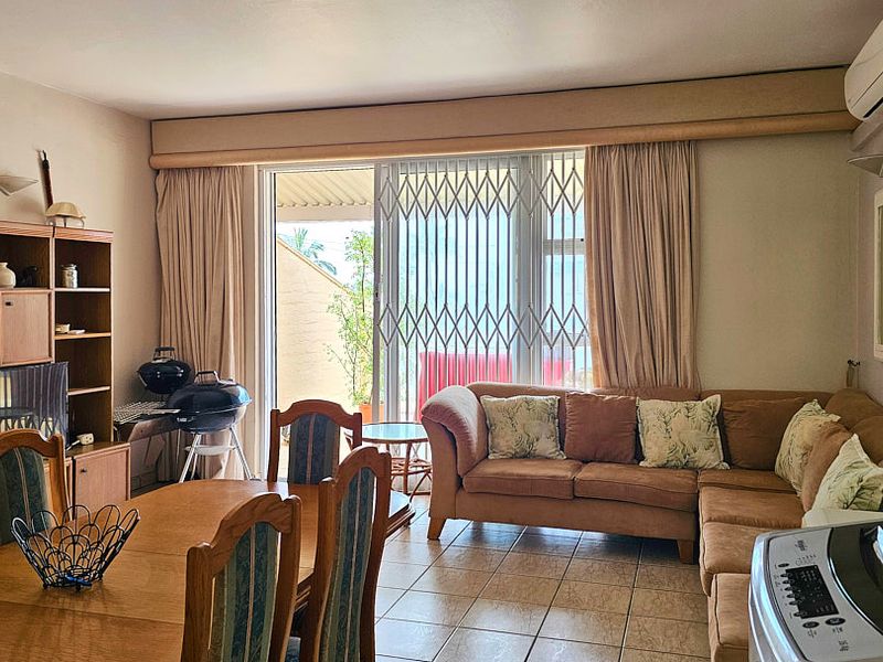 Open-plan living and dining area featuring tiled flooring, a wall-mounted air conditioner, and sliding door access to an outdoor patio space.