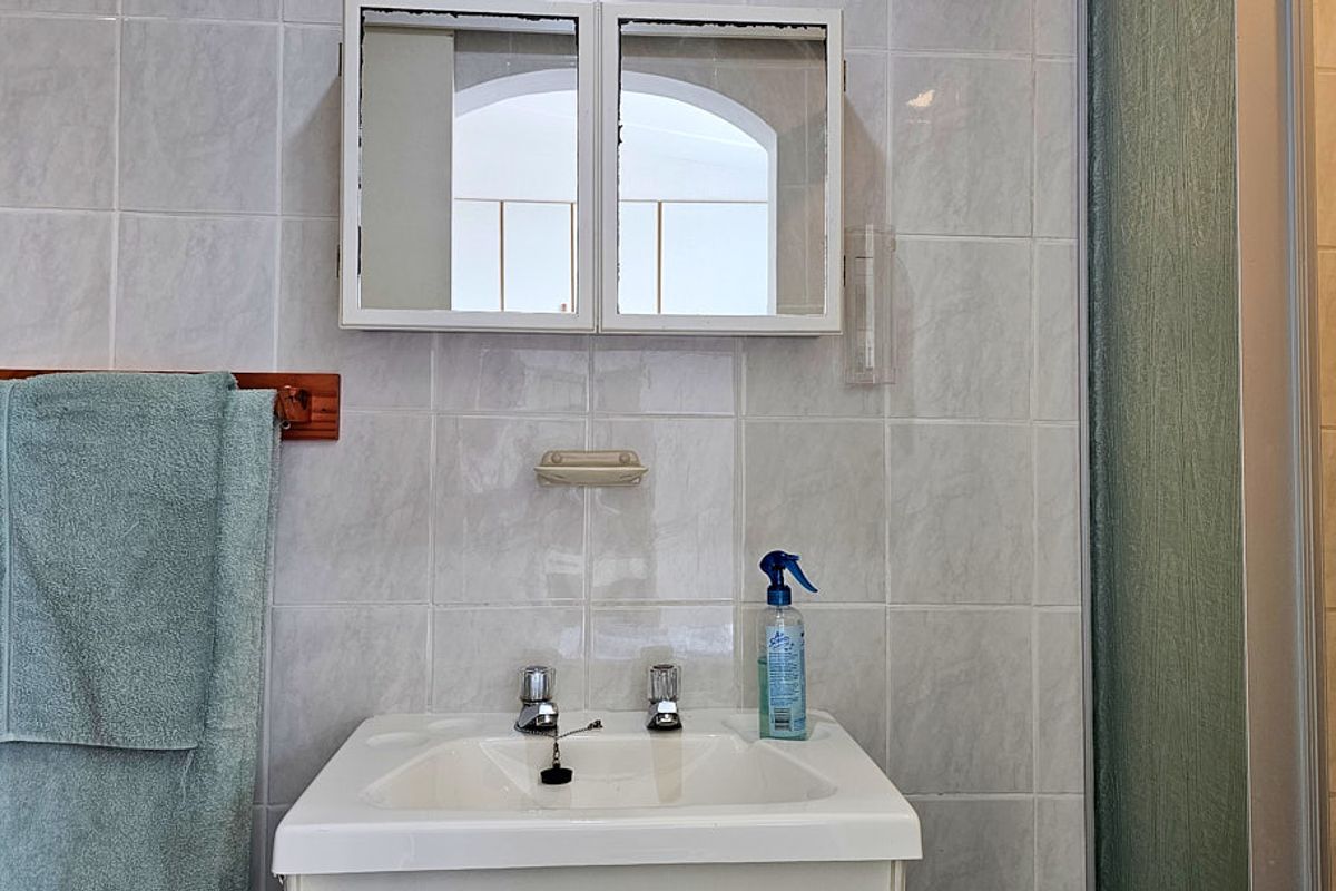 A functional bathroom featuring a wall-mounted medicine cabinet, ceramic basin with chrome taps, and tiled wall finishes.