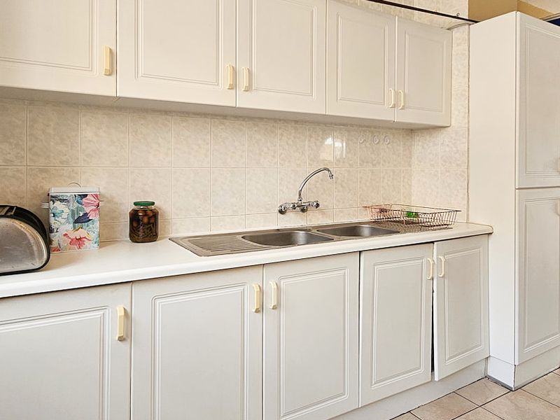 A functional kitchen featuring white laminate cabinetry, a double bowl stainless steel sink, tiled splashback, and tiled flooring.