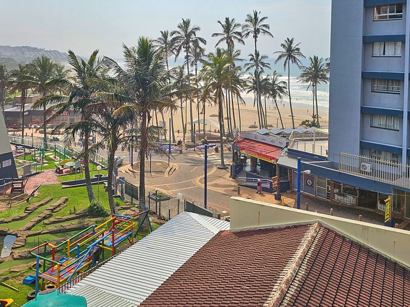 Elevated coastal view overlooking the beach, palm trees, and surrounding apartment complex grounds.