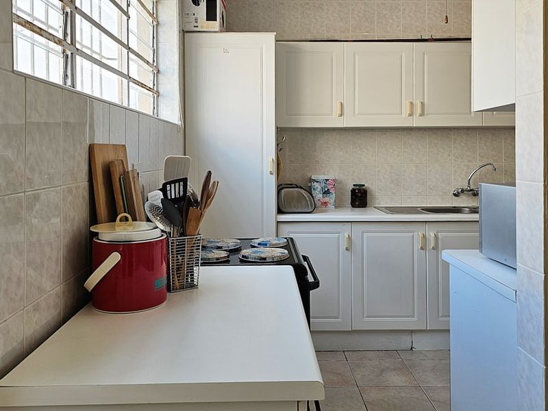 A functional kitchen featuring white built-in cabinetry, tiled backsplash, and tiled flooring, with a window fitted with security bars.