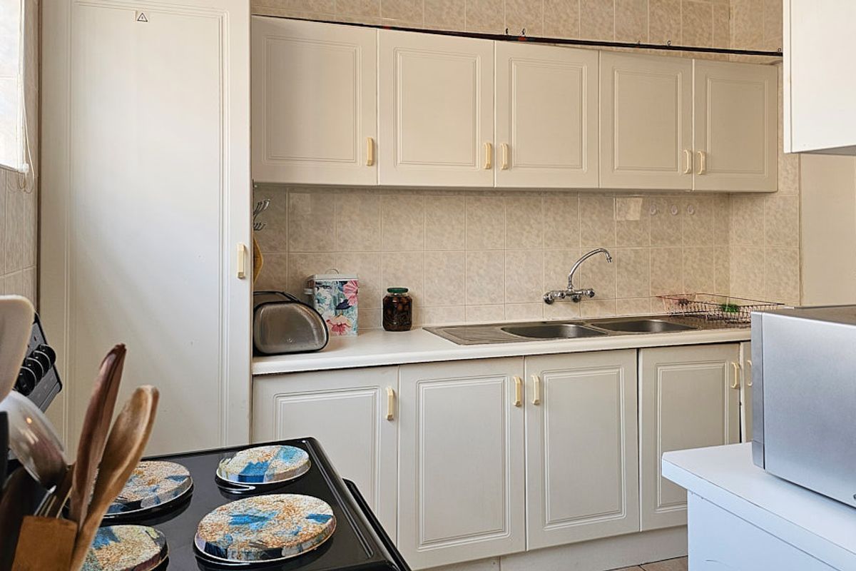 A functional kitchen featuring white built-in cabinetry, a double basin sink, and a tiled backsplash, offering a classic layout with potential for modernization.