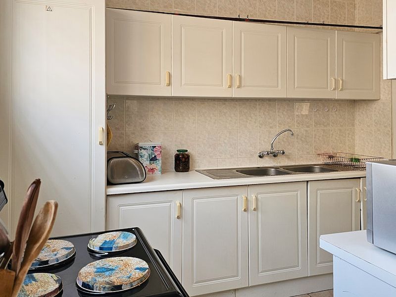 A functional kitchen featuring white built-in cabinetry, a double basin sink, and a tiled backsplash, offering a classic layout with potential for modernization.