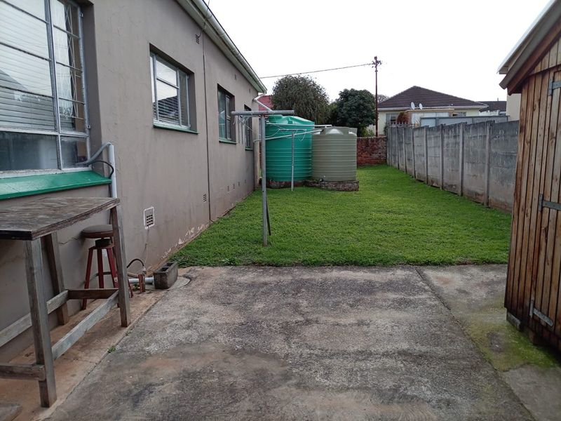 Rear exterior view featuring a concrete patio, lawn area, water storage tanks, and perimeter precast concrete walling.