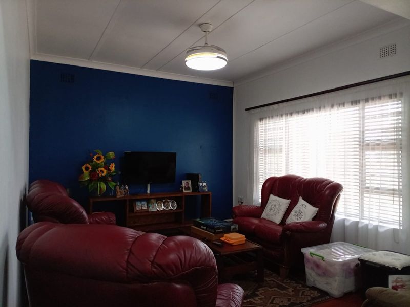 A comfortable living room featuring a bold blue accent wall, large window with venetian blinds, and a central ceiling fan.