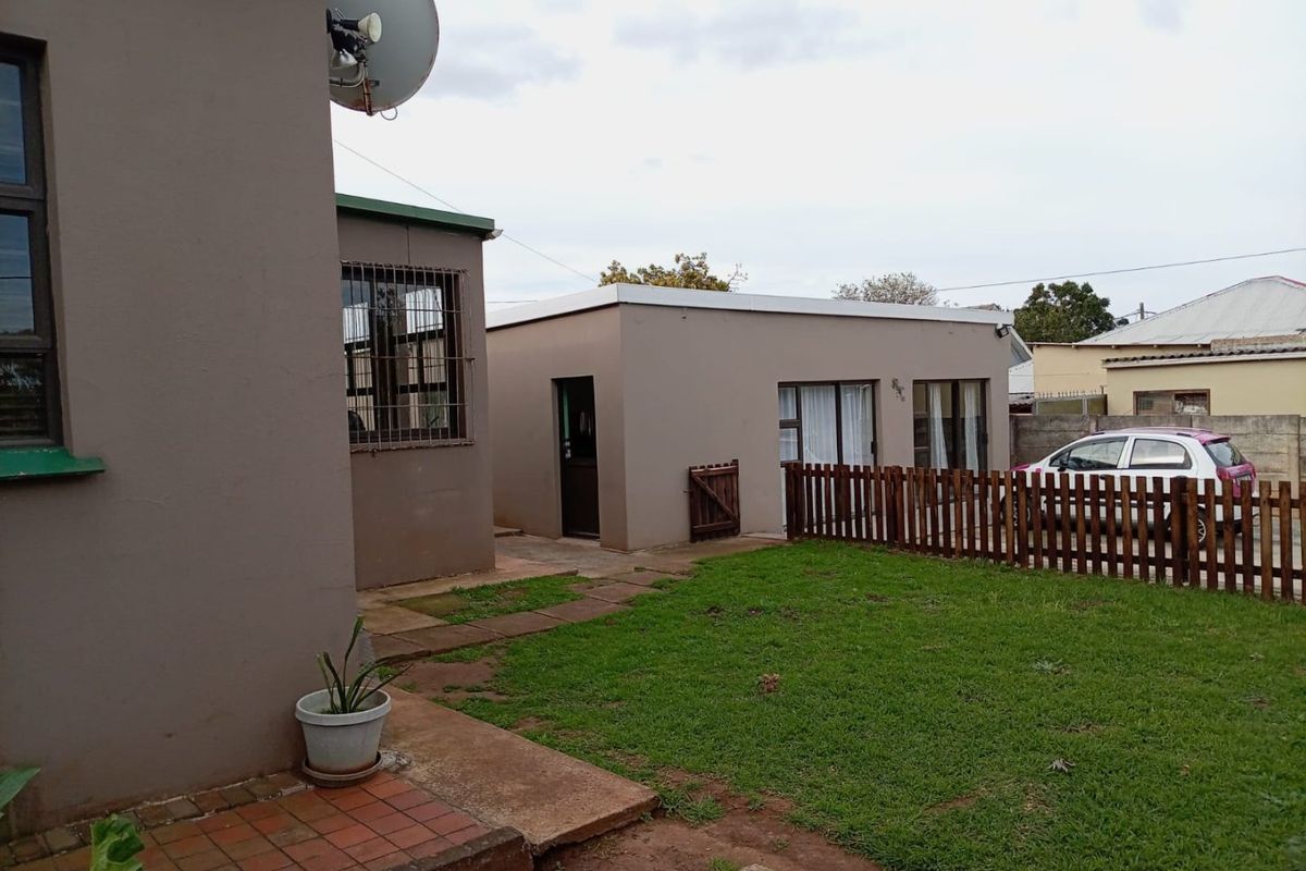 Rear exterior view of the property featuring a small lawn, paved walkway, and a wooden fence separating the garden area.