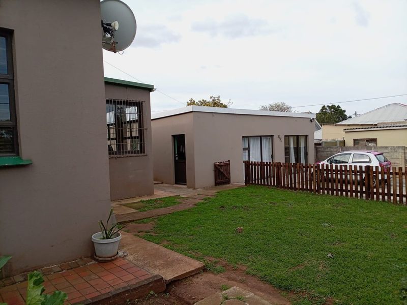 Rear exterior view of the property featuring a small lawn, paved walkway, and a wooden fence separating the garden area.