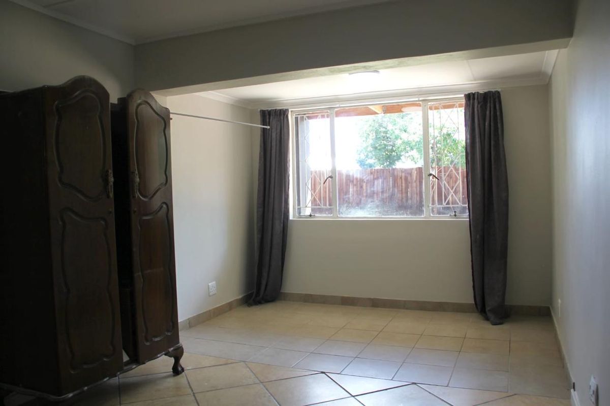 A spacious, neutrally painted bedroom featuring tiled flooring and a large window with security bars, offering a blank canvas for personalization.