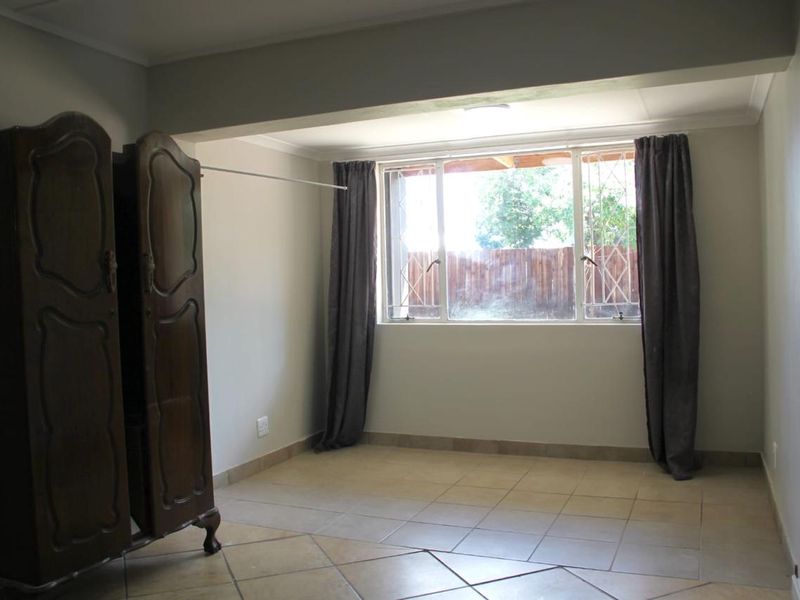 A spacious, neutrally painted bedroom featuring tiled flooring and a large window with security bars, offering a blank canvas for personalization.