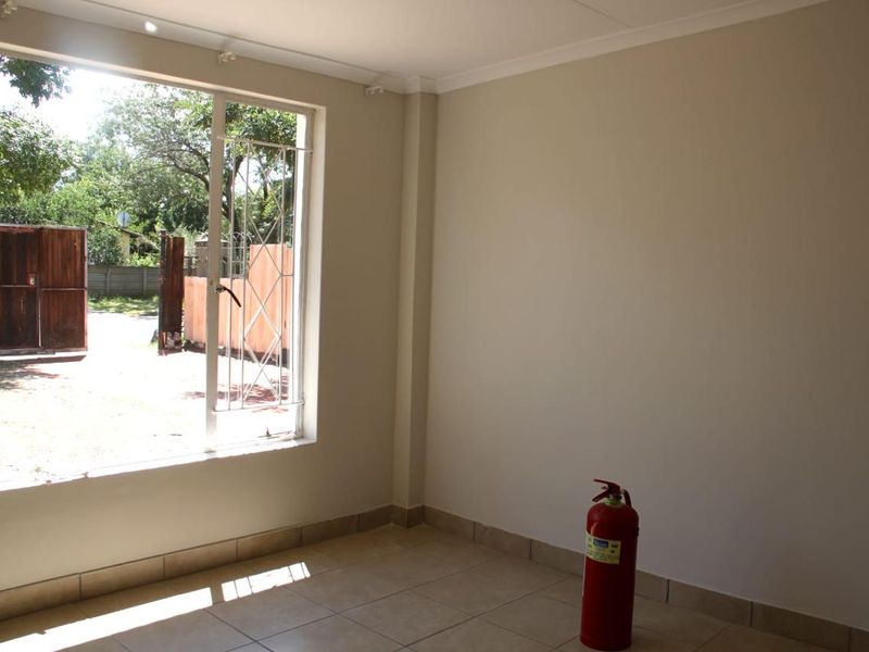 A bright, empty living area featuring tiled flooring, neutral walls, and a large window with security bars overlooking the exterior.