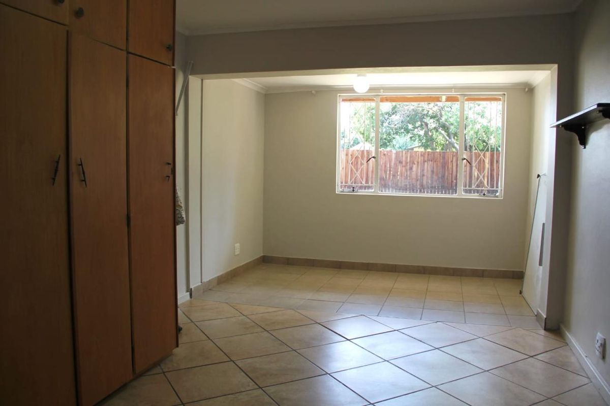 An empty living area featuring tiled flooring, built-in wooden cupboards, and a window with security bars, offering a neutral space ready for personalization.