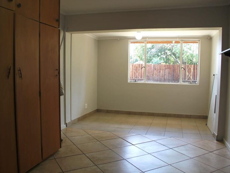 An empty living area featuring tiled flooring, built-in wooden cupboards, and a window with security bars, offering a neutral space ready for personalization.