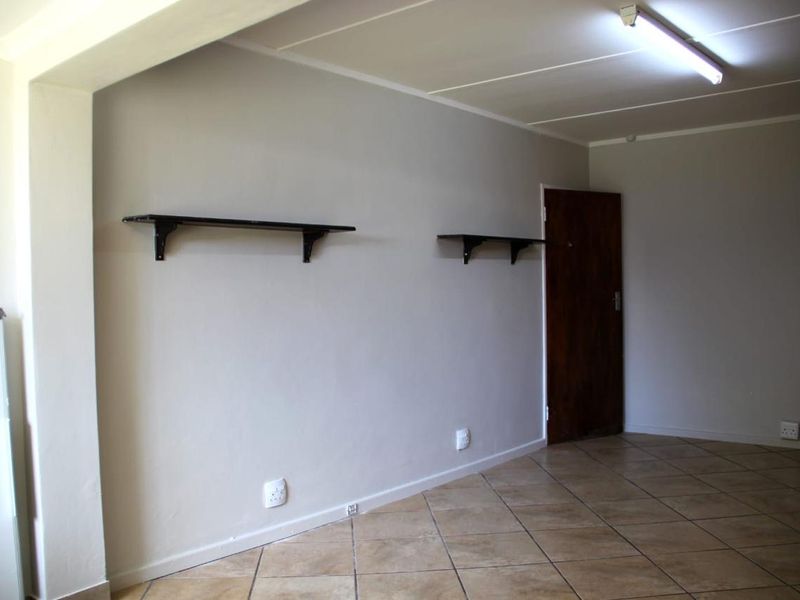 An empty living area featuring neutral wall paint, tiled flooring, and wall-mounted shelving units.