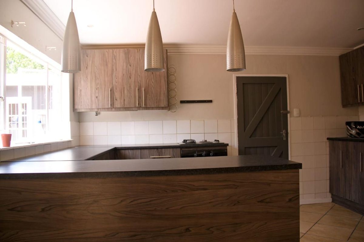 A functional kitchen featuring wood-look cabinetry, dark laminate countertops, a gas hob, and tiled backsplash, offering a clean and practical workspace.