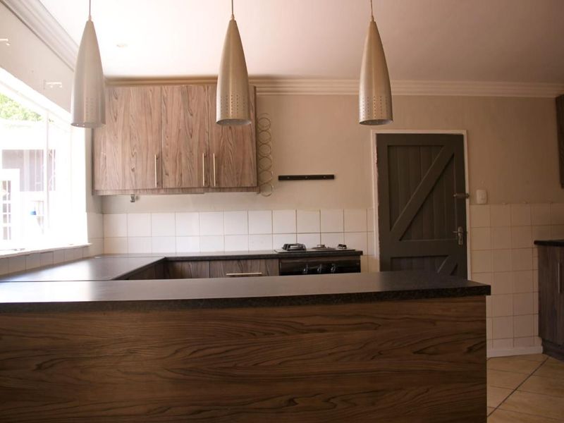 A functional kitchen featuring wood-look cabinetry, dark laminate countertops, a gas hob, and tiled backsplash, offering a clean and practical workspace.