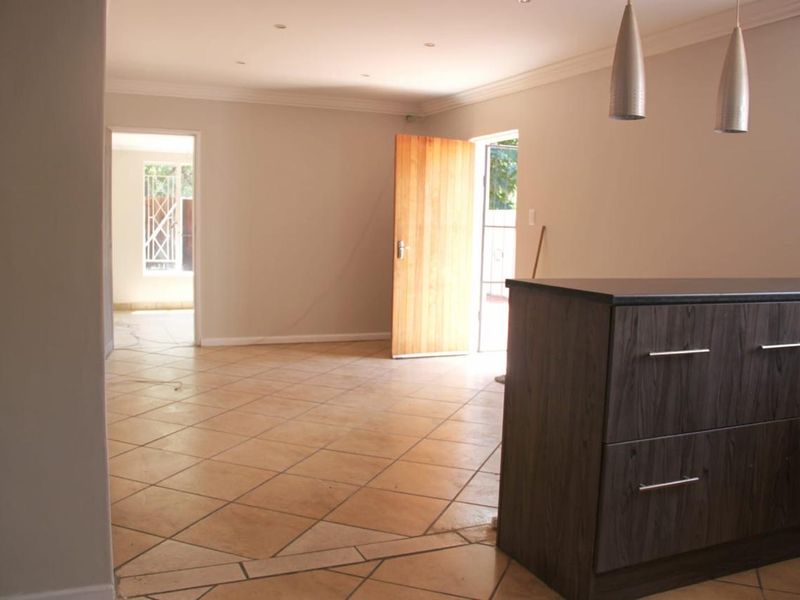 An open-plan living area featuring tiled flooring, a modern kitchen island, and recessed lighting, leading to an adjacent room and outdoor access.
