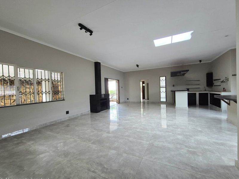 Spacious open-plan living and kitchen area featuring large format floor tiles, a built-in fireplace, a skylight, and modern kitchen cabinetry.