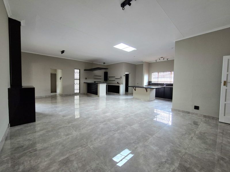 Spacious open-plan living and kitchen area featuring large format floor tiles, a modern kitchen island, built-in cabinetry, and a contemporary freestanding fireplace.