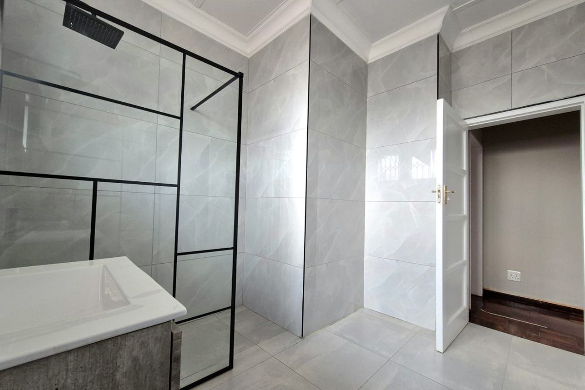 Modern bathroom featuring large-format grey marble-look wall tiles, a walk-in shower with a black-framed glass screen, and a contemporary vanity basin.