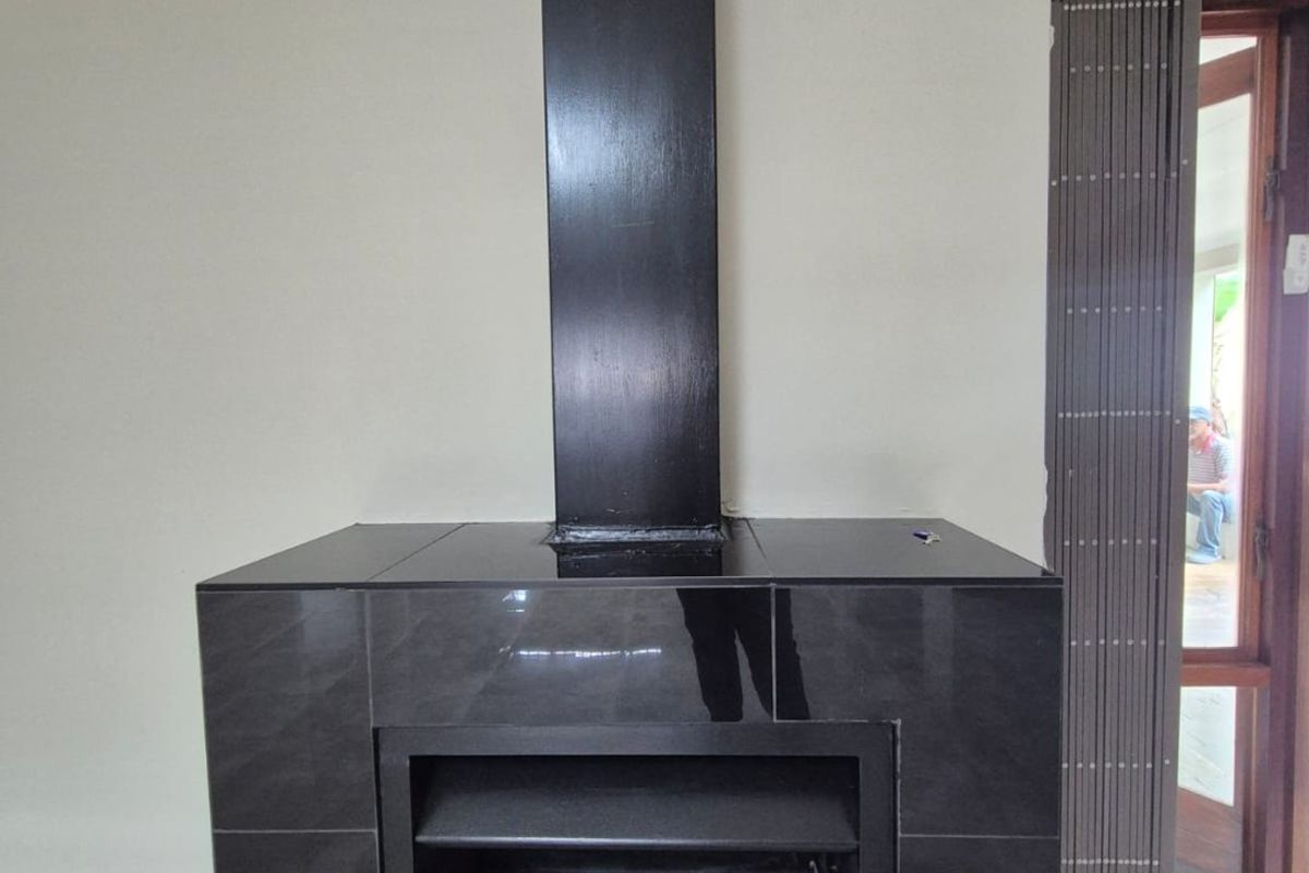 A modern living area featuring a sleek, black built-in fireplace with a matching chimney flue and neutral tiled flooring.