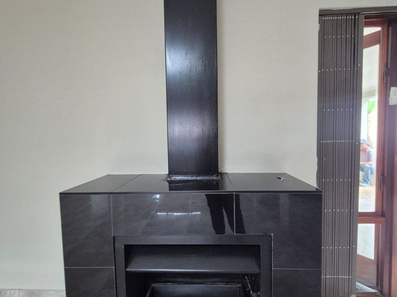 A modern living area featuring a sleek, black built-in fireplace with a matching chimney flue and neutral tiled flooring.