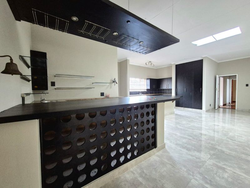 Spacious open-plan living area featuring a built-in bar with overhead glass storage, modern tiled flooring, and ample built-in cabinetry.
