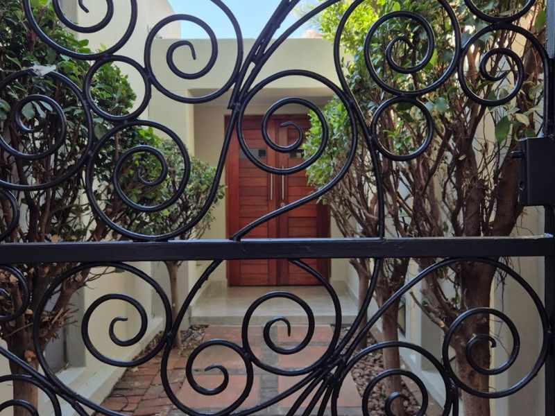 A secure entrance featuring a decorative wrought iron gate leading to a paved walkway and a solid wooden double front door.