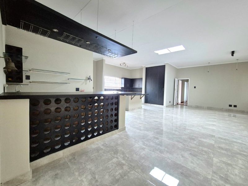Spacious open-plan living area featuring a built-in bar with overhead glass storage, modern tiled flooring, and ample natural light from a skylight.