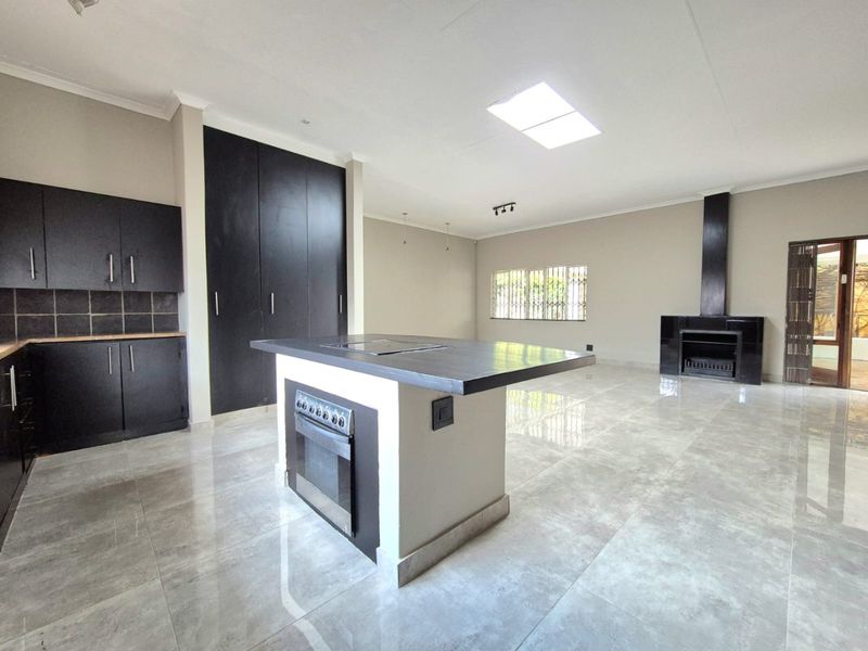 Spacious open-plan living area featuring a modern kitchen with a central island, built-in oven, fireplace, and large format floor tiles.