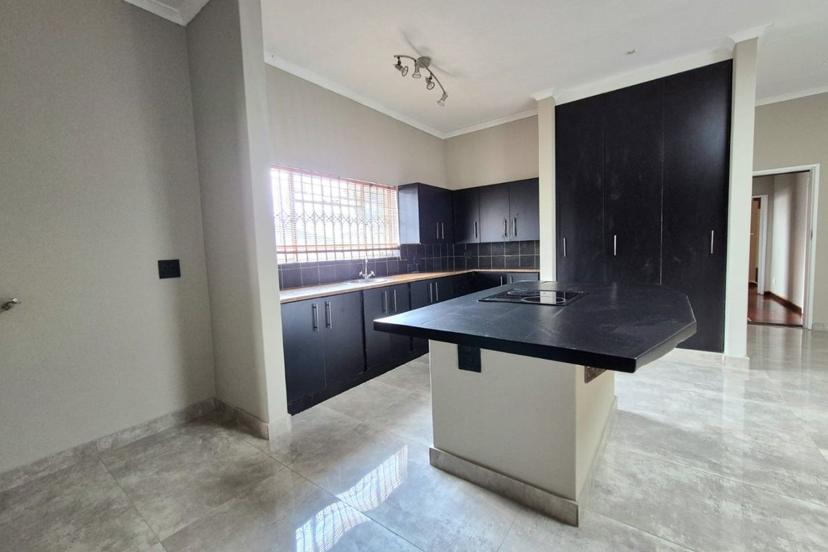 Modern kitchen featuring dark cabinetry, a central island with a built-in hob, tiled flooring, and ample storage space.