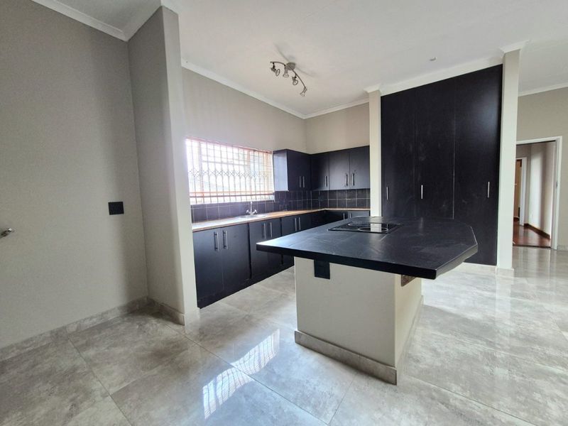 Modern kitchen featuring dark cabinetry, a central island with a built-in hob, tiled flooring, and ample storage space.