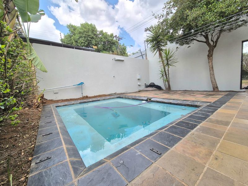 Outdoor pool area featuring a paved patio surround, perimeter wall with electric fencing, and established trees in a private backyard setting.