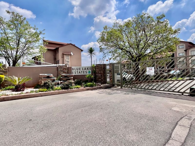The entrance to Blue Lake Estates featuring a secure automated gate, electric fencing, and well-maintained landscaped garden beds with stone feature walls.