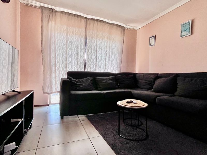 A living room featuring tiled flooring, neutral wall finishes, and large window access with curtain tracks, providing a functional and comfortable living space.