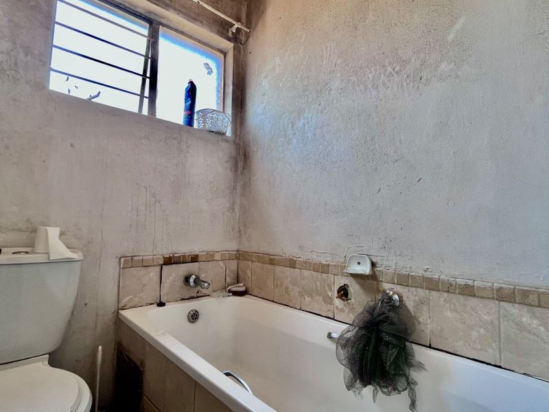A bathroom in need of renovation, featuring a bathtub, toilet, and tiled splashback with visible wall surface damage.