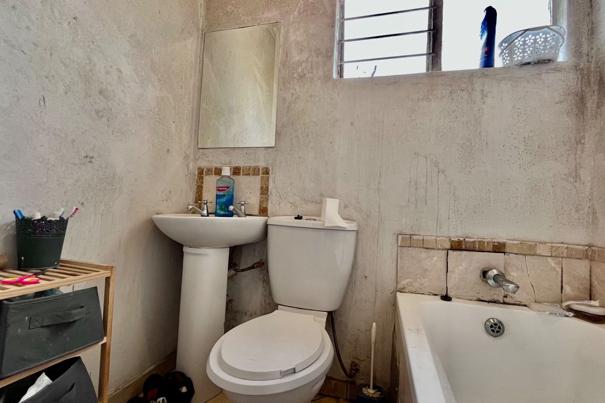 A compact bathroom featuring a pedestal basin, toilet, and bathtub, requiring significant cosmetic renovation and wall surface repairs to improve its condition.