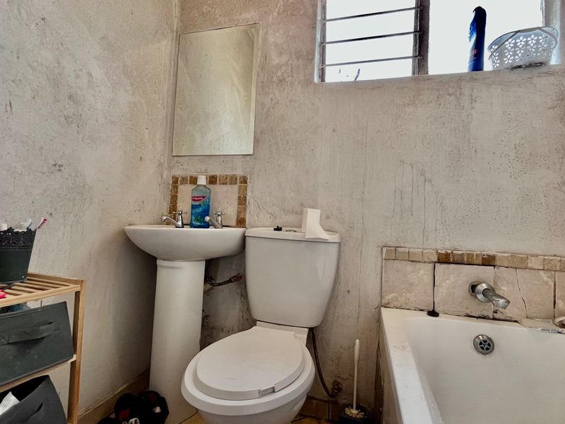 A compact bathroom featuring a pedestal basin, toilet, and bathtub, requiring significant cosmetic renovation and wall surface repairs to improve its condition.