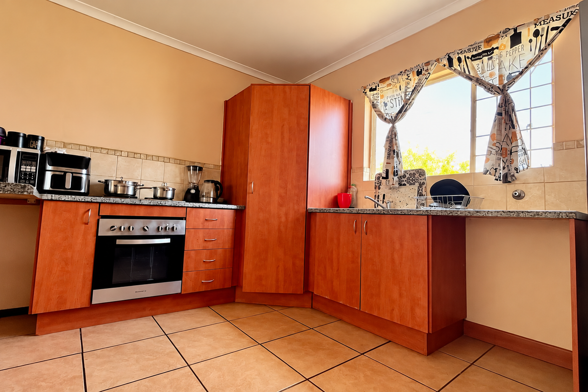 A functional kitchen featuring wooden cabinetry, granite countertops, a built-in oven, and tiled flooring, offering a practical layout with ample storage space.
